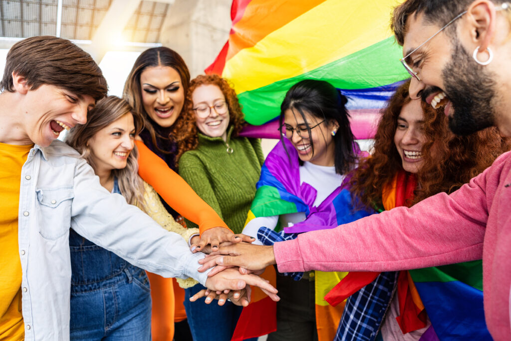 Homosexual diverse group of young people stacking hands together outdoors. LGBTQ community concept with multiracial friends celebrating gay pride festival day.